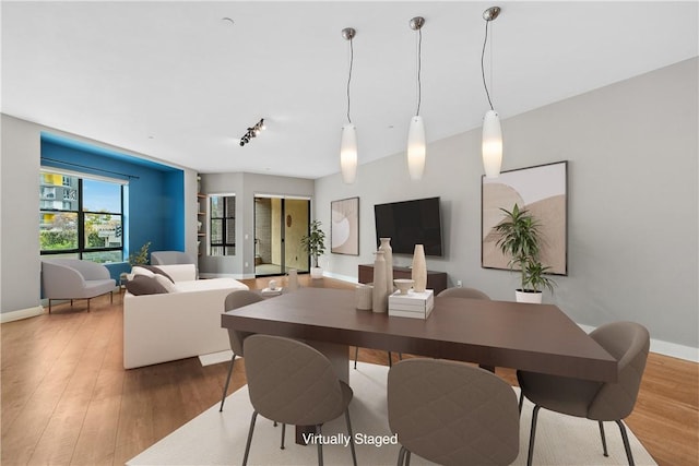 dining area with baseboards, wood finished floors, and track lighting