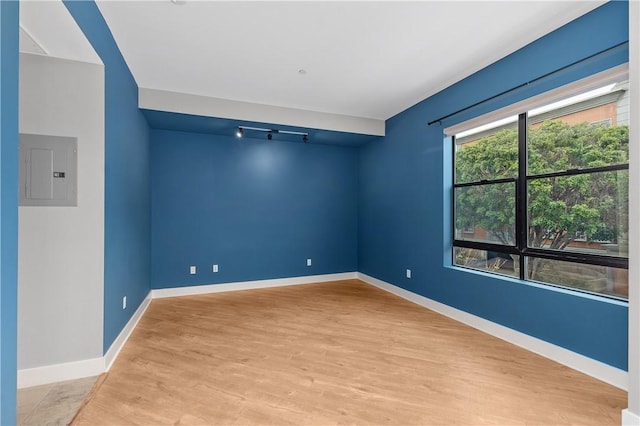 empty room with electric panel, wood finished floors, and baseboards