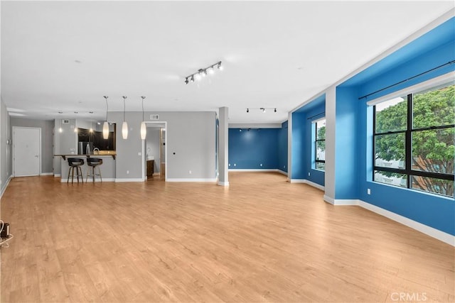 unfurnished living room with light wood-style flooring, rail lighting, and baseboards