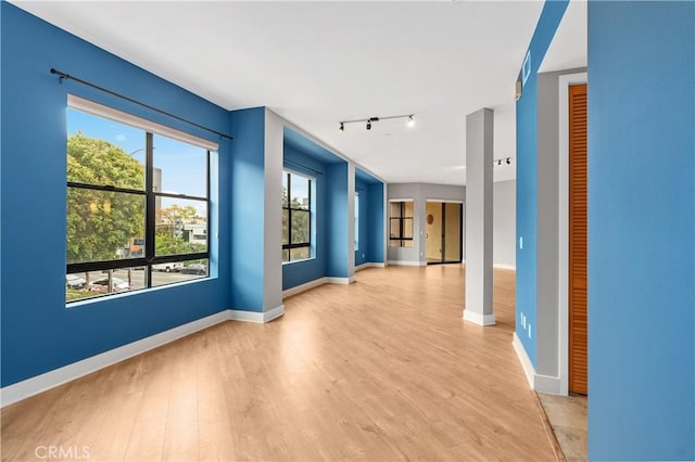 unfurnished room with track lighting, light wood-style flooring, and baseboards