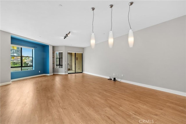 unfurnished living room featuring rail lighting, light wood-type flooring, and baseboards