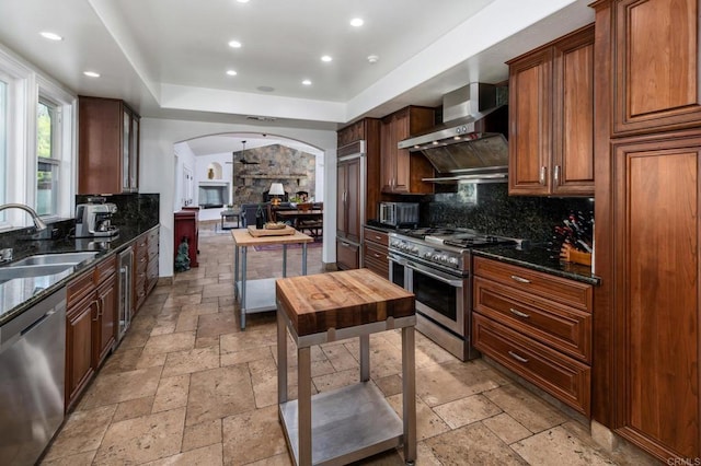 35715 Calle Nopal, Temecula, CA 92592 - kitchen with appliances with stainless steel finishes, wall chimney range hood, stone tile floors, arched walkways, and tasteful backsplash