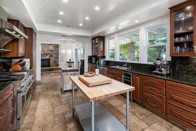 35715 Calle Nopal, Temecula, CA 92592 - kitchen with appliances with stainless steel finishes, beverage cooler, stone tile floors, arched walkways, and wall chimney exhaust hood