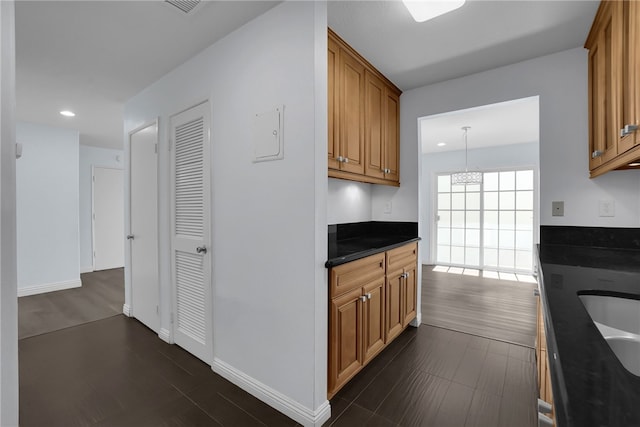 kitchen featuring dark countertops, recessed lighting, dark wood finished floors, and brown cabinetry