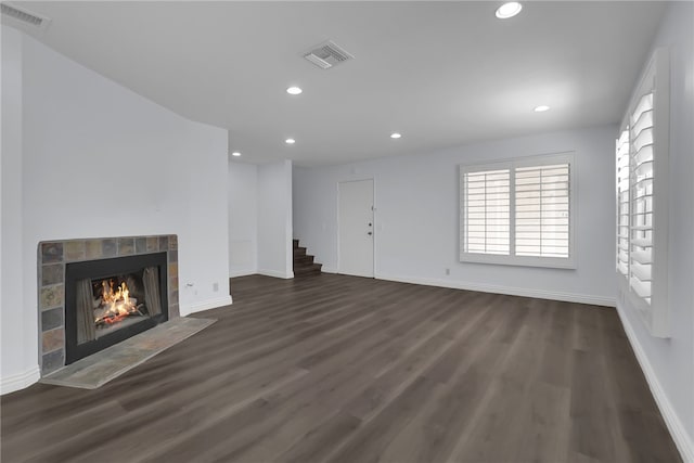 unfurnished living room featuring a tiled fireplace, visible vents, stairs, and dark wood-type flooring