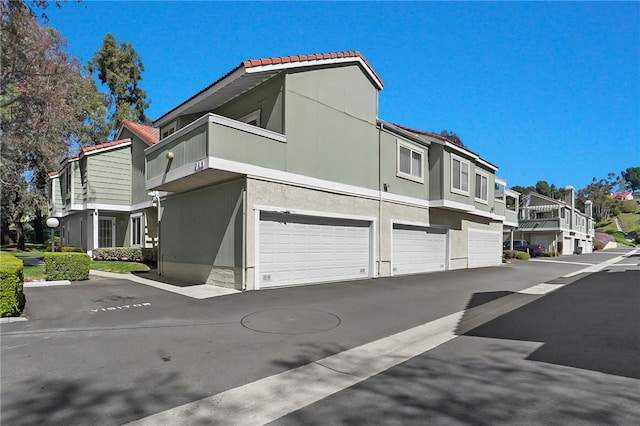 view of property exterior featuring a balcony, a garage, a residential view, and stucco siding