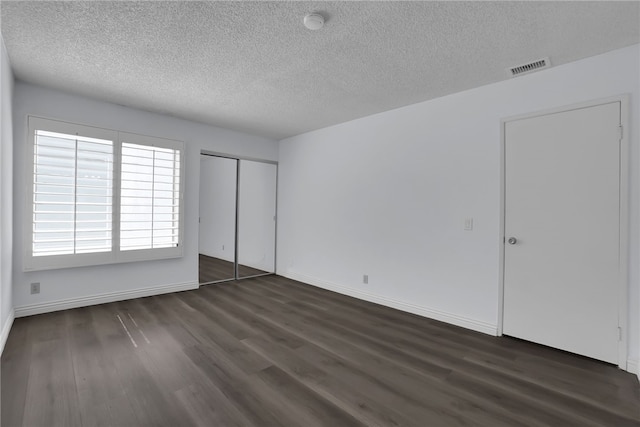 unfurnished bedroom with visible vents, a textured ceiling, and dark wood-style floors