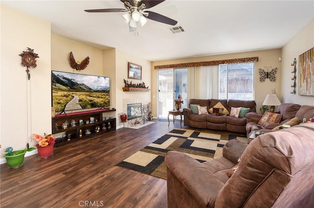 living area featuring ceiling fan, visible vents, wood finished floors, and a tiled fireplace