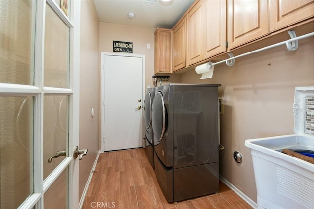 clothes washing area with washing machine and dryer, cabinet space, light wood-type flooring, and baseboards