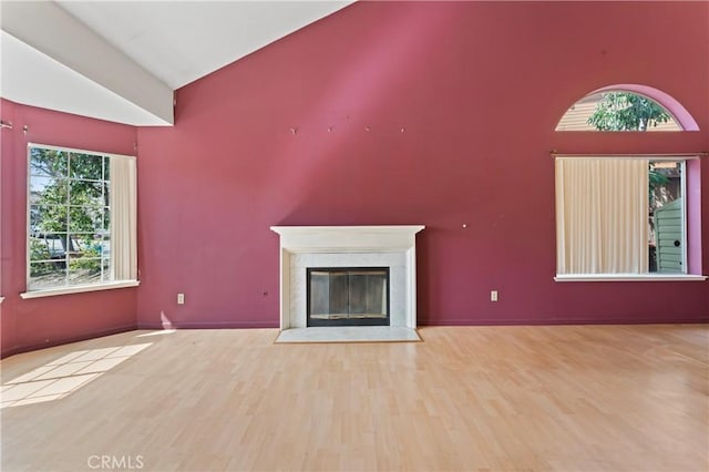 unfurnished living room with vaulted ceiling, wood finished floors, and a high end fireplace