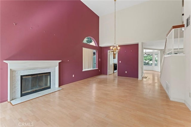 unfurnished living room with a high end fireplace, a chandelier, light wood-style flooring, and visible vents