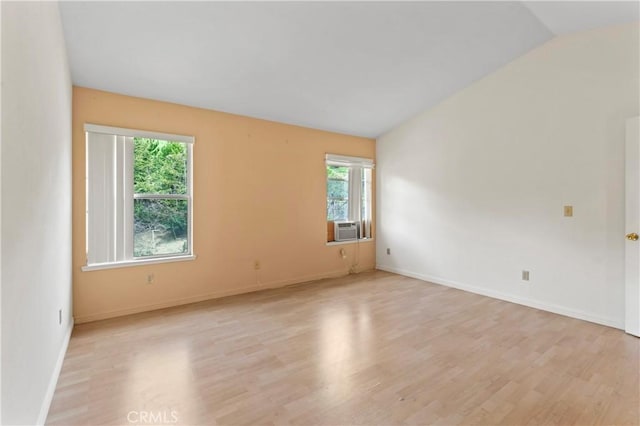 empty room with vaulted ceiling, cooling unit, baseboards, and light wood-type flooring