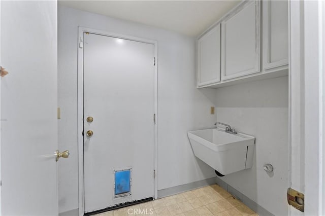 washroom featuring cabinet space, baseboards, light floors, and a sink