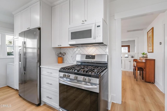 kitchen featuring stainless steel appliances, backsplash, light wood-style flooring, and white cabinetry