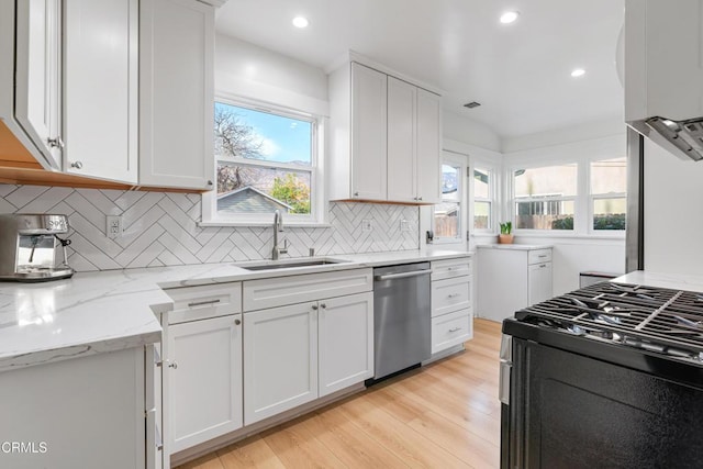 kitchen featuring a sink, light stone counters, white cabinetry, light wood-style floors, and appliances with stainless steel finishes