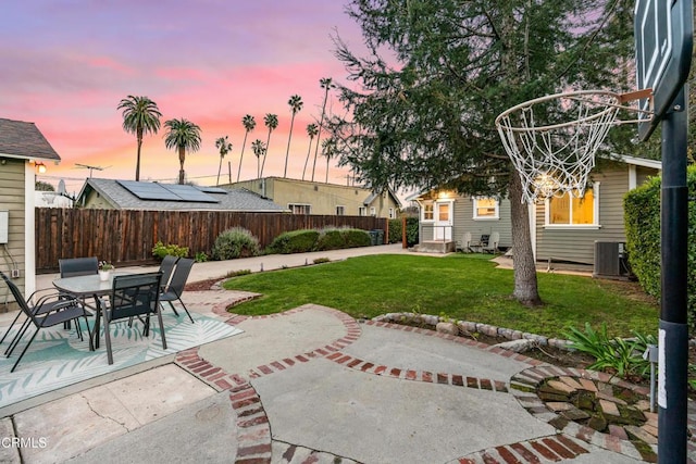 patio terrace at dusk with a yard, central AC, and fence