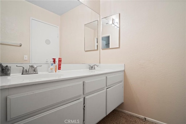 full bathroom with a sink, baseboards, double vanity, and a textured wall