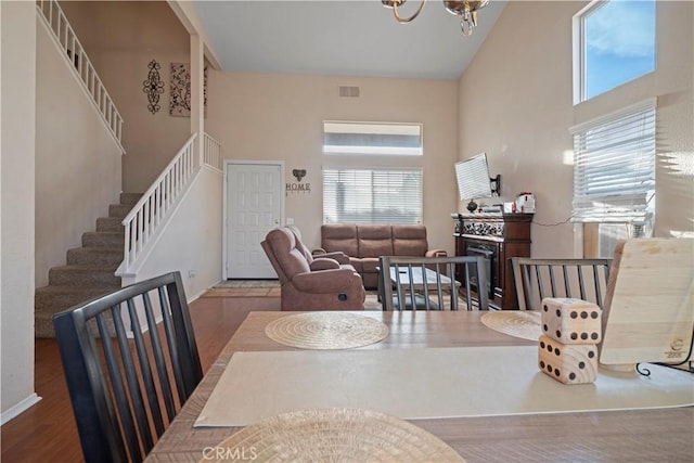 dining room featuring stairway, wood finished floors, visible vents, a towering ceiling, and a notable chandelier