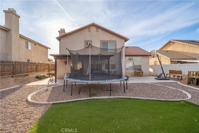 rear view of property with stucco siding, a patio, a trampoline, and a fenced backyard