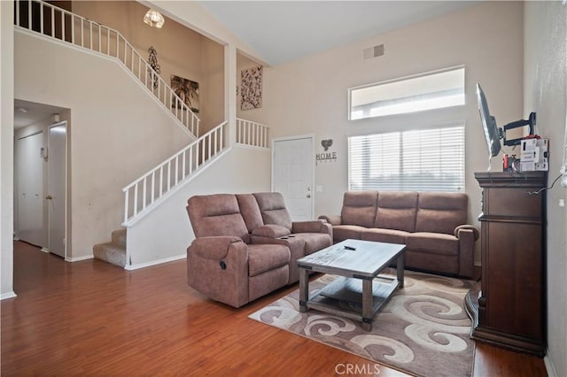 living room featuring wood finished floors, visible vents, baseboards, a high ceiling, and stairs