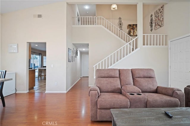 living room featuring stairs, a high ceiling, wood finished floors, and visible vents