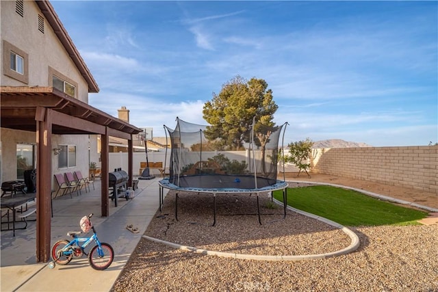 view of yard featuring a patio, a trampoline, a fenced backyard, and a mountain view