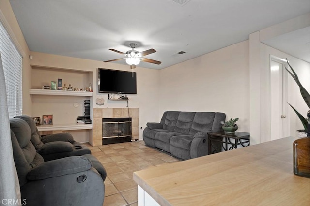 living room featuring light tile patterned floors, built in features, a fireplace, and ceiling fan