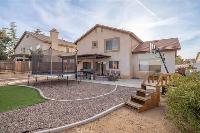 back of property featuring a patio area, a trampoline, a fenced backyard, and stucco siding