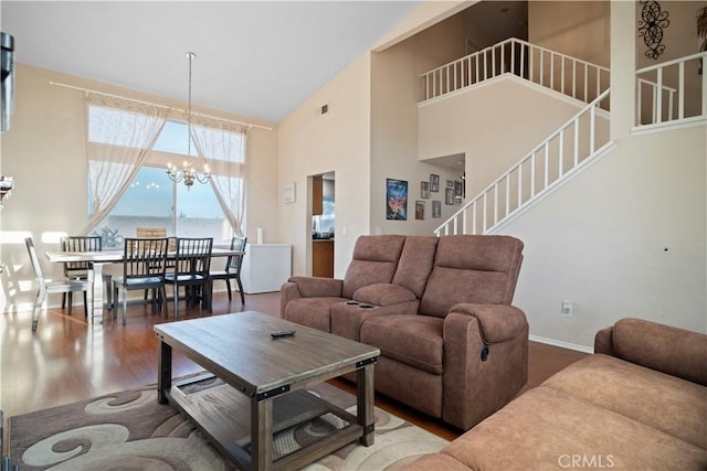 living area with a notable chandelier, wood finished floors, baseboards, a towering ceiling, and stairs