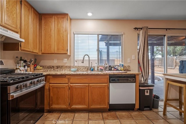 kitchen featuring stainless steel gas stove, under cabinet range hood, a sink, white dishwasher, and light stone countertops