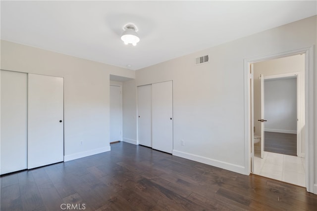 unfurnished bedroom featuring dark wood finished floors, visible vents, baseboards, and multiple closets