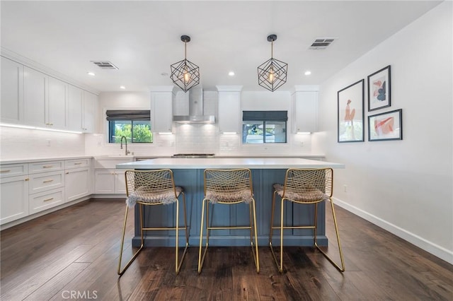 kitchen with tasteful backsplash, visible vents, wall chimney range hood, light countertops, and white cabinetry