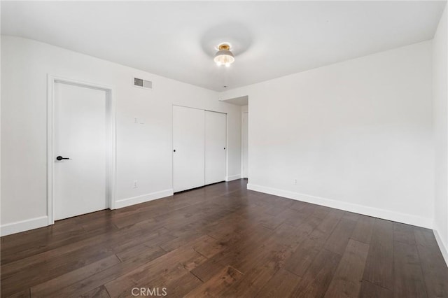 unfurnished bedroom with visible vents, baseboards, dark wood-type flooring, and a closet