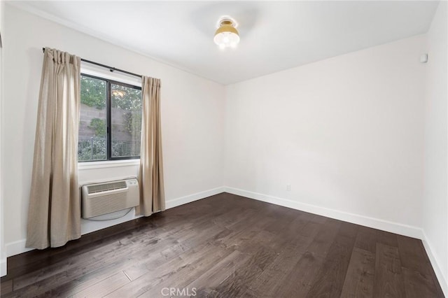 empty room with a wall unit AC, baseboards, and dark wood-type flooring