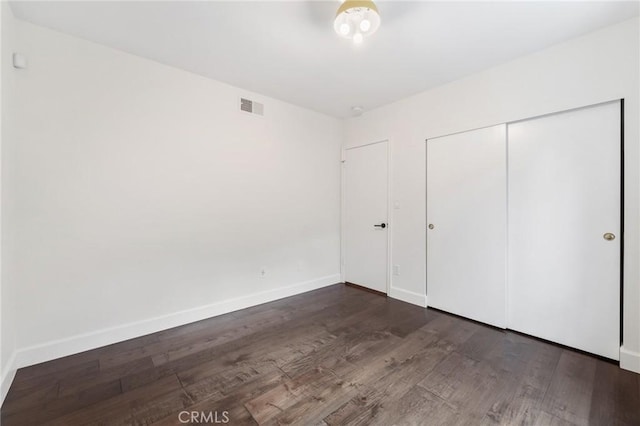 unfurnished bedroom featuring visible vents, baseboards, a closet, and wood finished floors