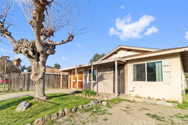 ranch-style house with a front yard, fence, and stucco siding