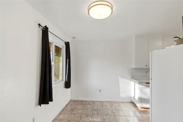 interior space with baseboards, light countertops, light tile patterned floors, freestanding refrigerator, and white cabinetry