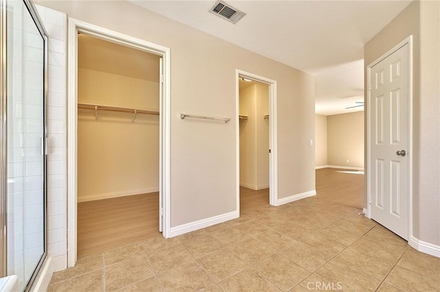 unfurnished bedroom with a walk in closet, visible vents, a closet, light tile patterned floors, and baseboards