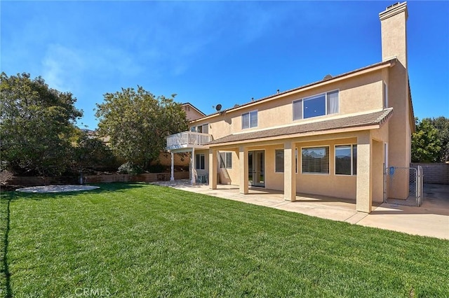 rear view of house with fence, stucco siding, a lawn, a chimney, and a patio