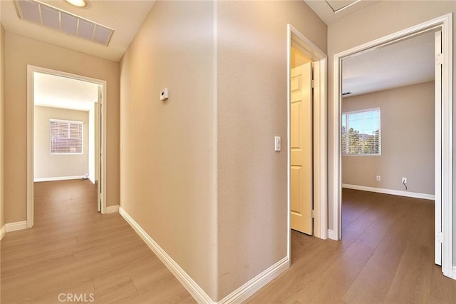 hallway featuring light wood finished floors, visible vents, and baseboards