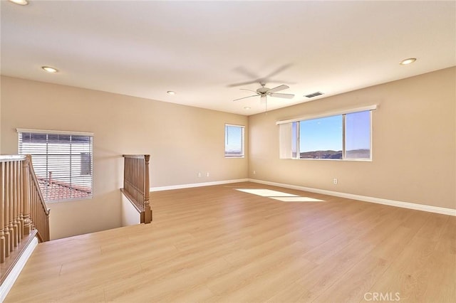 unfurnished room with visible vents, light wood-style flooring, a ceiling fan, and baseboards