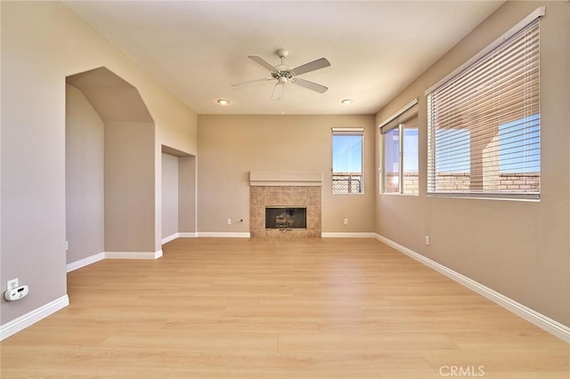 unfurnished living room featuring light wood-style flooring, a fireplace, baseboards, and ceiling fan