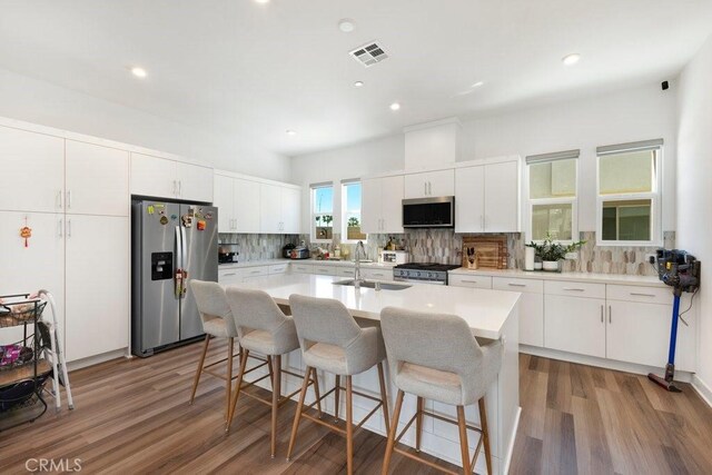 kitchen featuring visible vents, a breakfast bar area, decorative backsplash, stainless steel appliances, and a sink