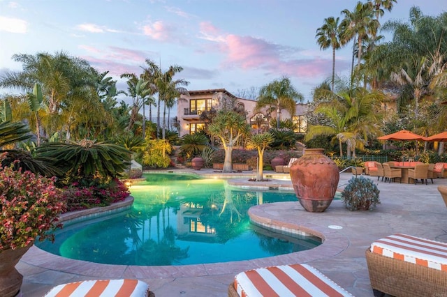 pool at dusk featuring an outdoor pool and a patio