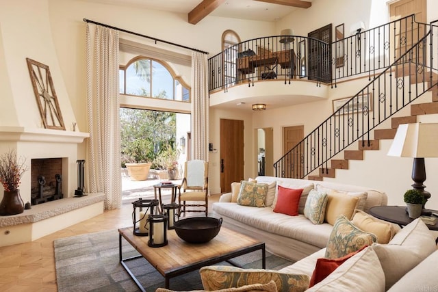 living room featuring beamed ceiling, a large fireplace, a towering ceiling, and stairs