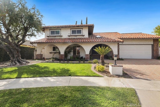 mediterranean / spanish-style home featuring stucco siding, a front lawn, a garage, a tiled roof, and decorative driveway