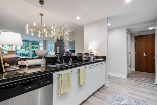 kitchen with light wood finished floors, dark stone counters, a sink, white cabinets, and dishwasher