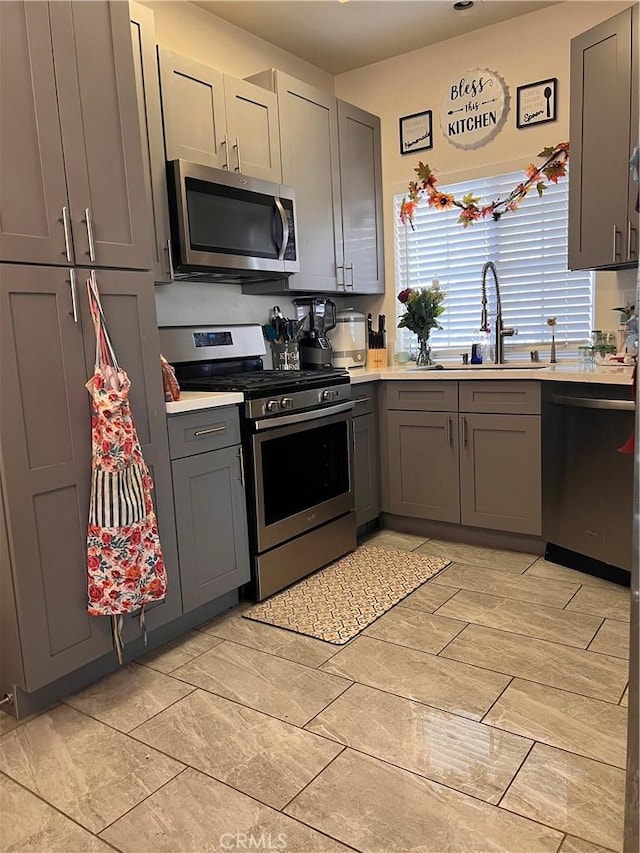 kitchen with light countertops, gray cabinets, appliances with stainless steel finishes, and a sink