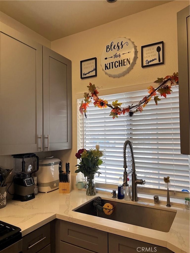 kitchen featuring a sink, light stone counters, and gray cabinetry