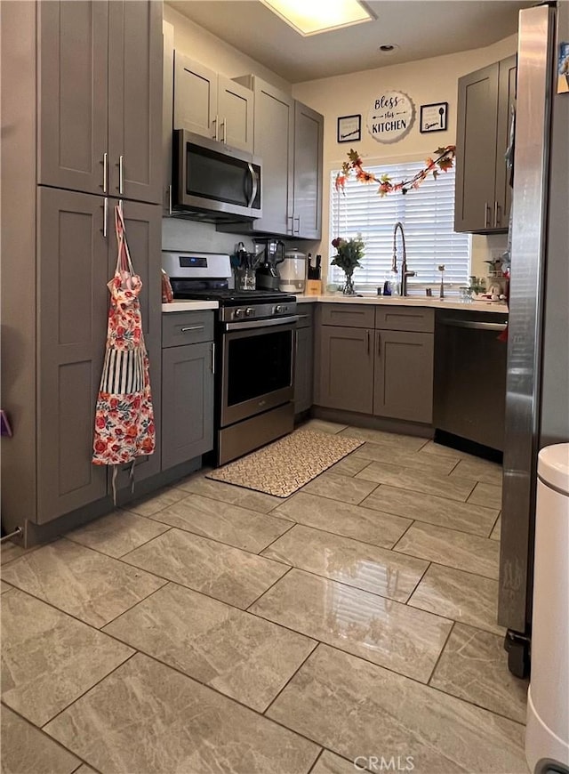 kitchen with gray cabinets, stainless steel appliances, light countertops, and a sink